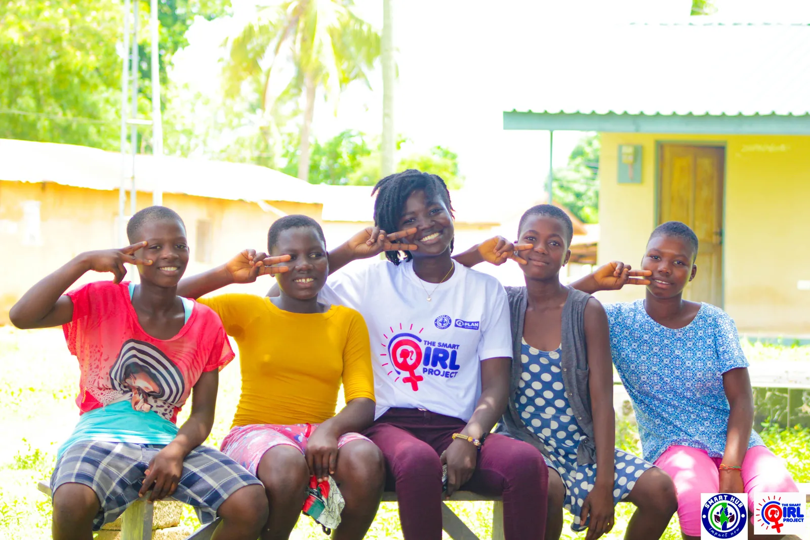 Five smiling girls and young women seated together outdoors.